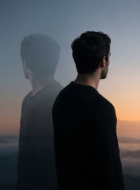 A man at sunset with his back turned, a translucent second self beside him