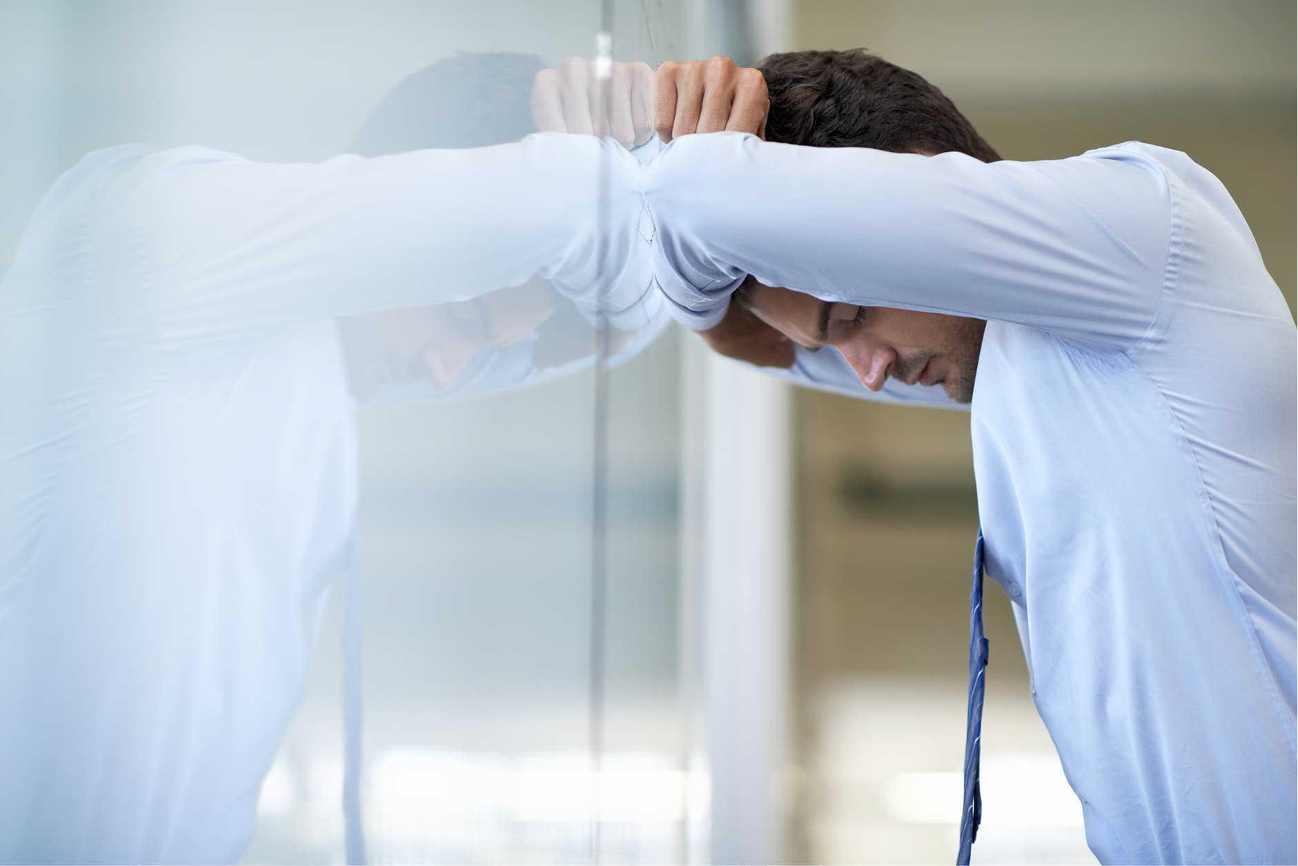 A man in a button-up shirt leaning his forehead against a glass partition